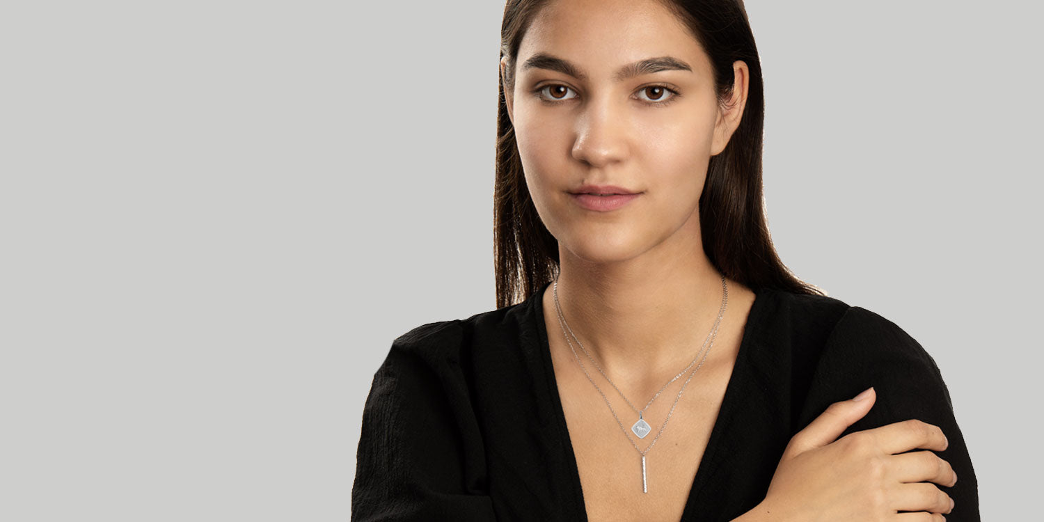 Junge Frau mit langen braunen Haaren trägt eine zarte Halskette mit rundem Anhänger vor grauem Hintergrund