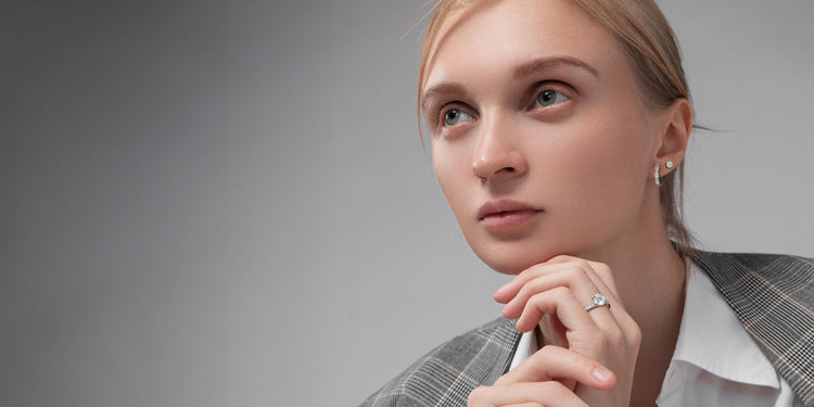 Blonde Frau in grauem Blazer trägt silbernen Ring mit Stein und kleine Ohrstecker