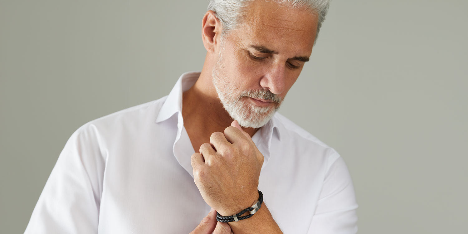 Eleganter Mann mit grauem Haar und Bart  in weißem Hemd trägt schwarzes Lederarmband